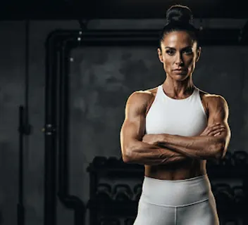 Muscular fitness athlete with arms crossed in a dark gym